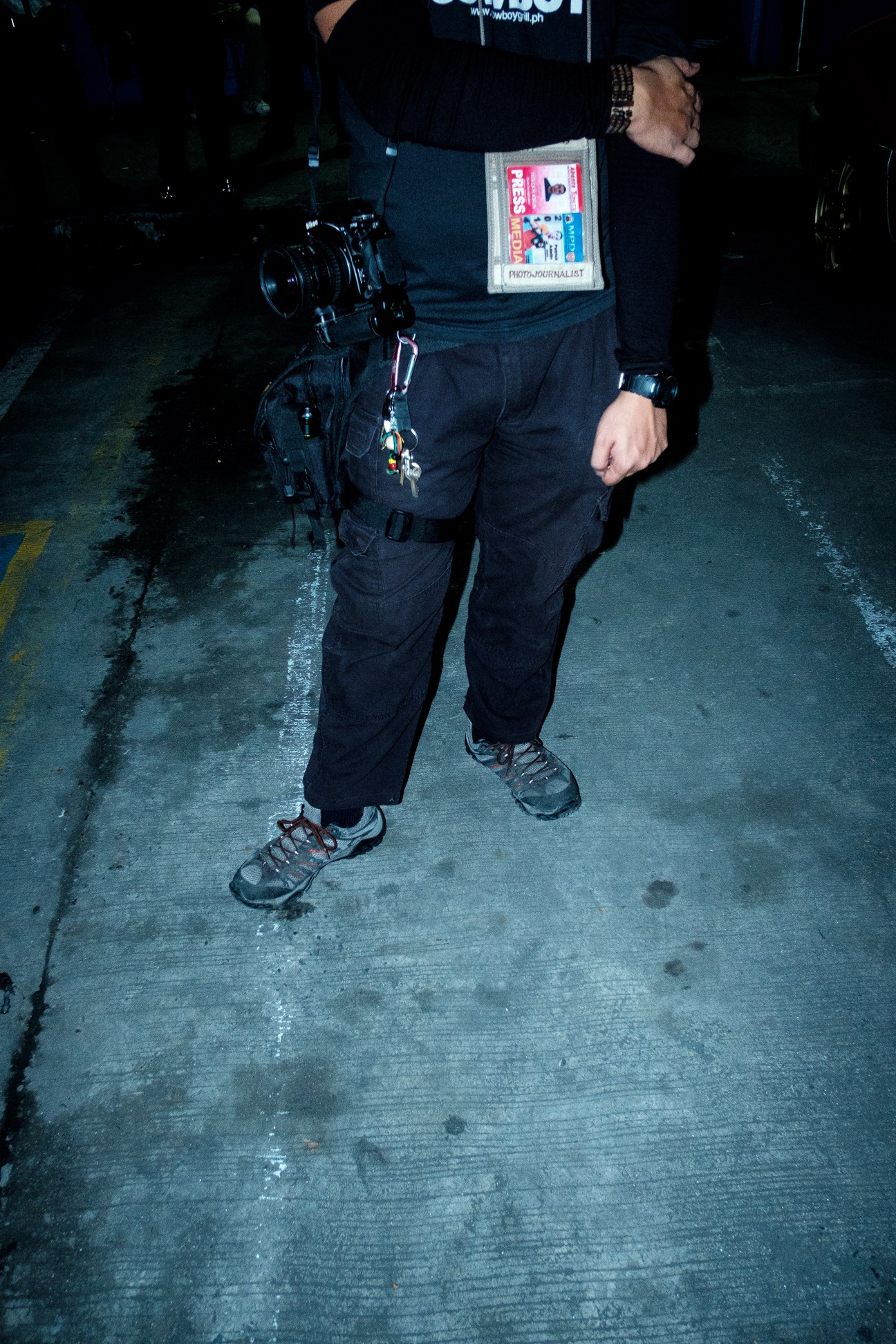 Photojournalist wearing press credentials and carrying camera equipment during night coverage of drug-related crime scenes in Manila.