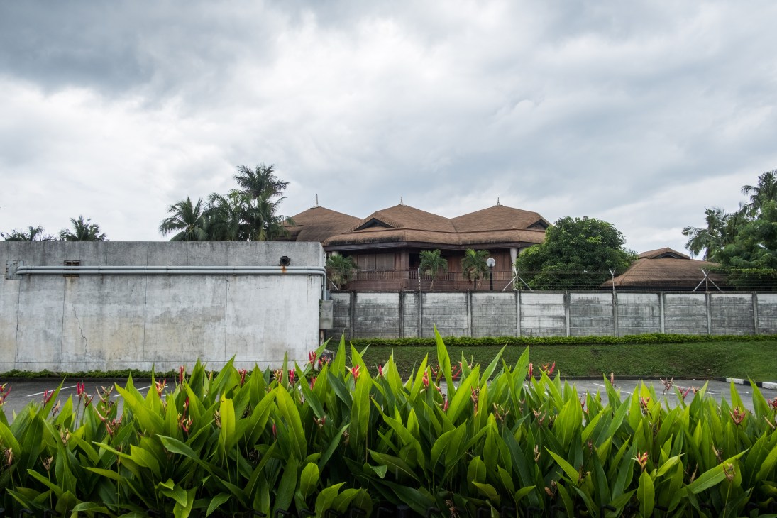 Coconut Palace, a government building in the Philippines, with distinctive brown rooflines behind concrete walls and tropical plants.