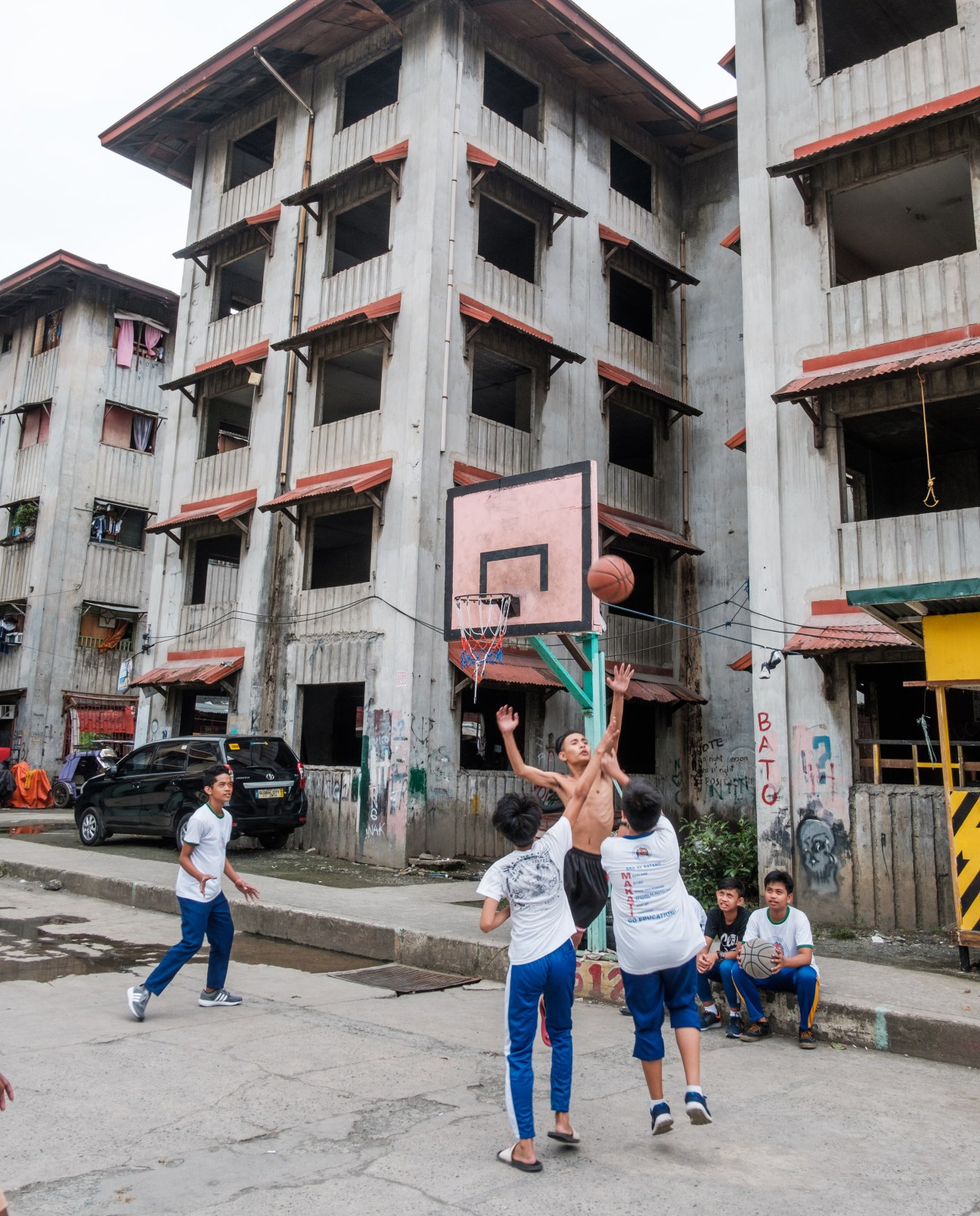 School children playing basketball in front of an unfinished concrete housing building in Makati City.