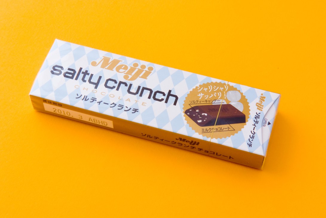 Meiji Salty Crunch chocolate bar with milk chocolate and salted candy pieces on yellow background.