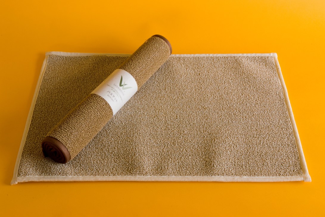 Sasawashi bath mat and rolled towel with product label on yellow background.