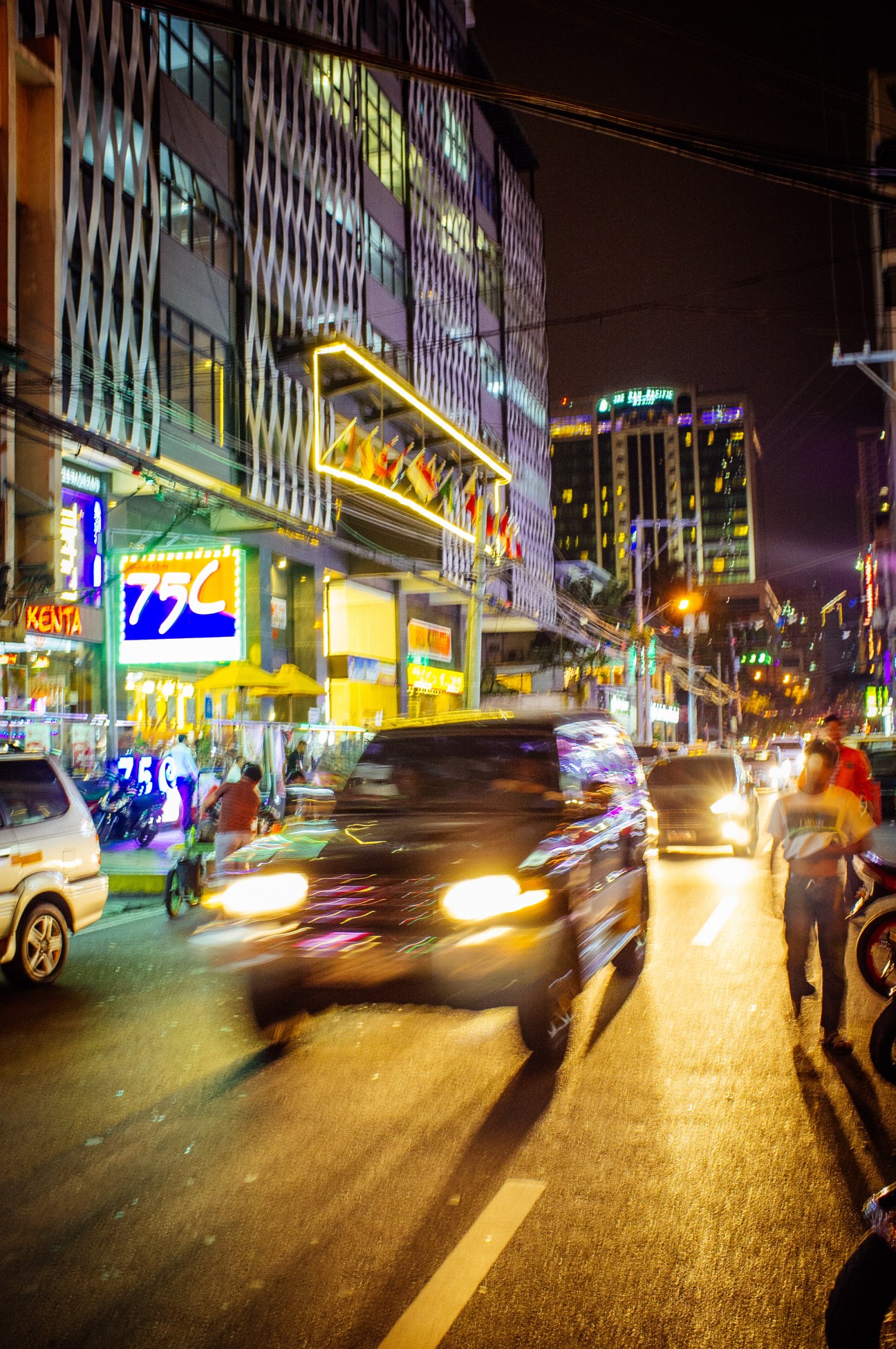 Night scene of Remedios Circle nightlife district with neon signs, moving vehicles, and illuminated buildings.