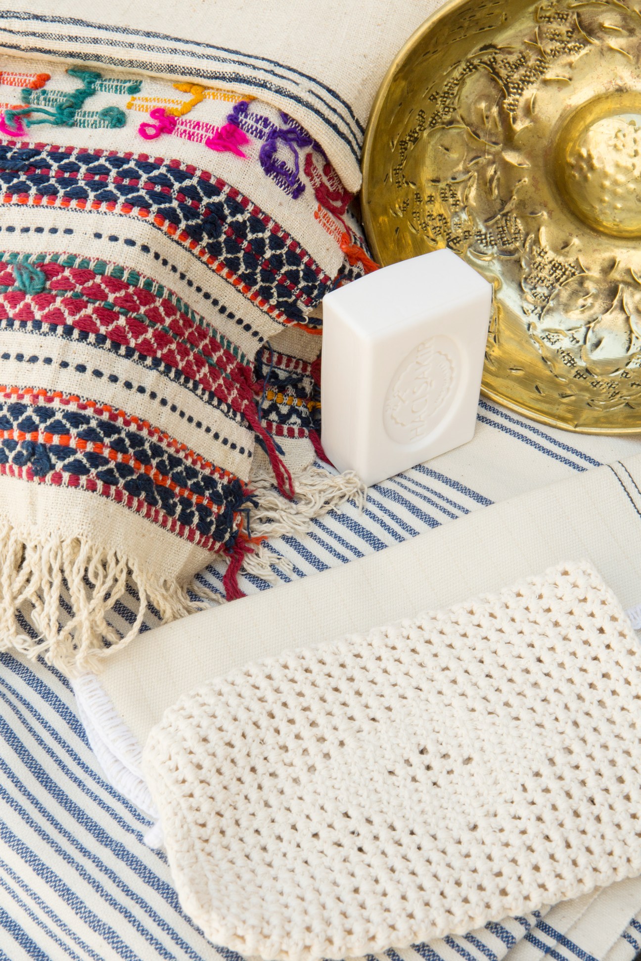 White soap bar and brass vessel displayed on colorful striped textile with woven patterns.