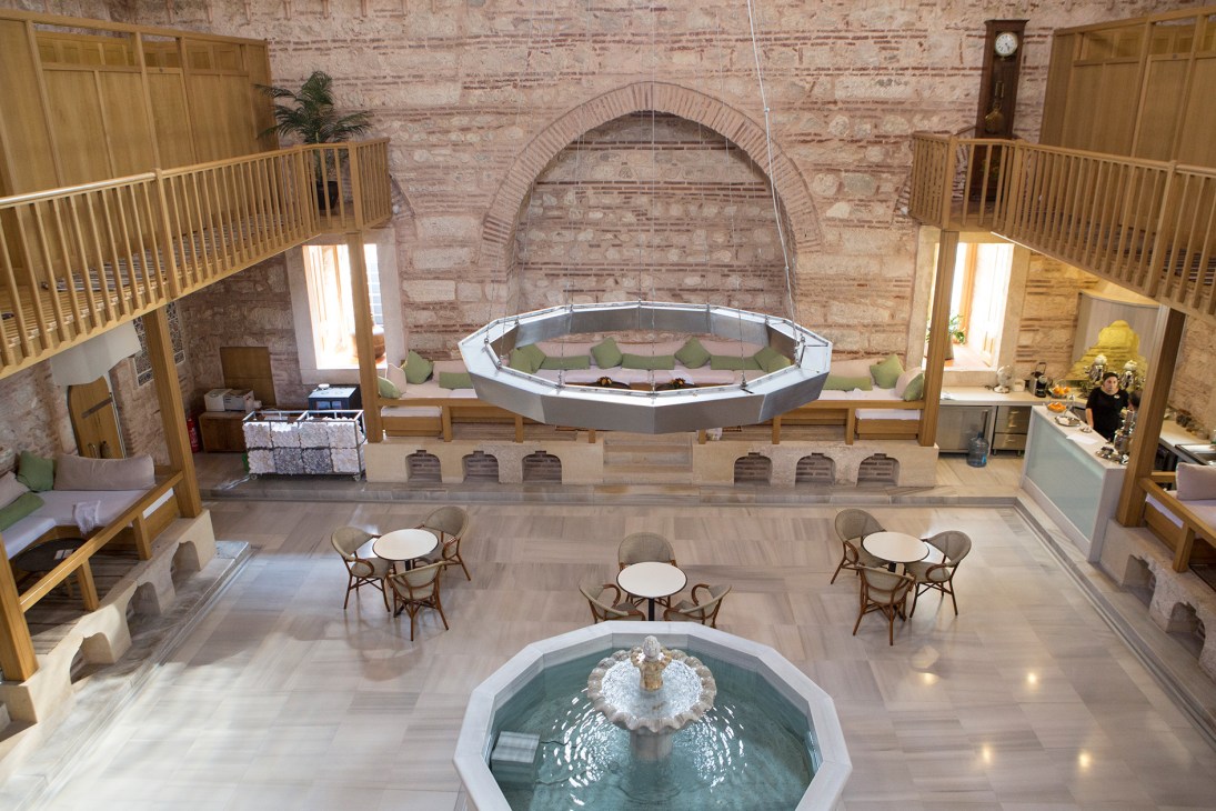 Interior of Kilic Ali Pasa Hamami spa in Istanbul showing marble platforms, fountain, arched brick ceiling and seating areas.