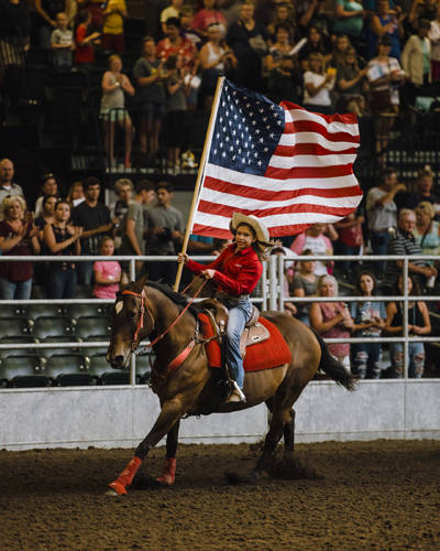 Person on horseback carrying an American flag at Iowa State Fair rodeo arena