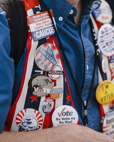 Political campaign badges and pins displaying voting messages and candidate names pinned to a person's clothing at Iowa State Fair.