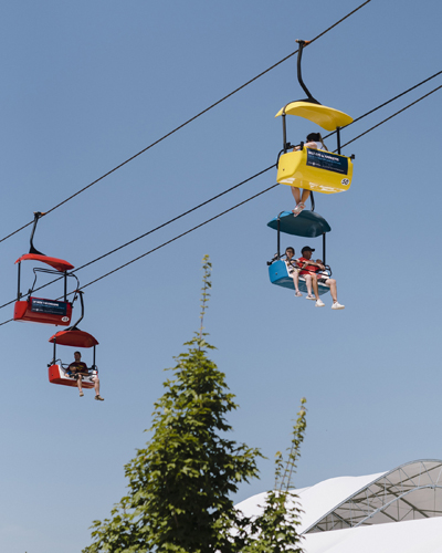 Colorful chair lift cars suspended on cables above Iowa State Fair grounds with trees below.