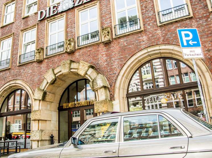 Façade of the Helmut-Schmidt-Haus in Hamburg with Die Zeit signage and a parked sedan.