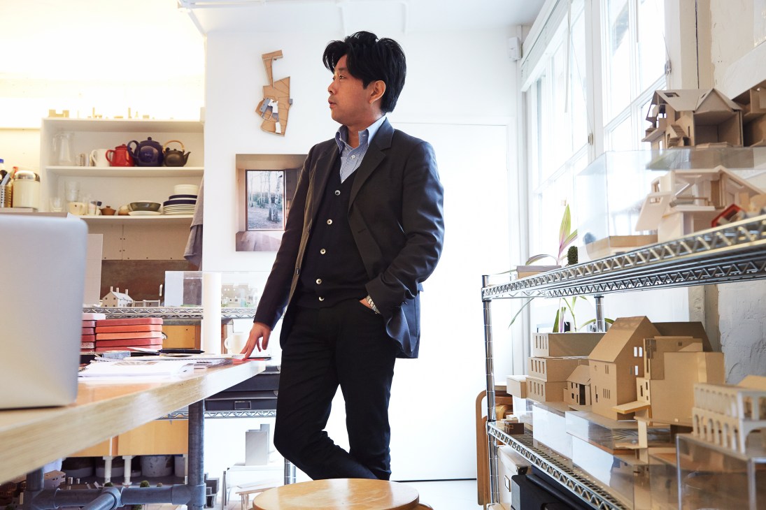Architect Takero Shimazaki stands in his studio surrounded by architectural models and sketches.