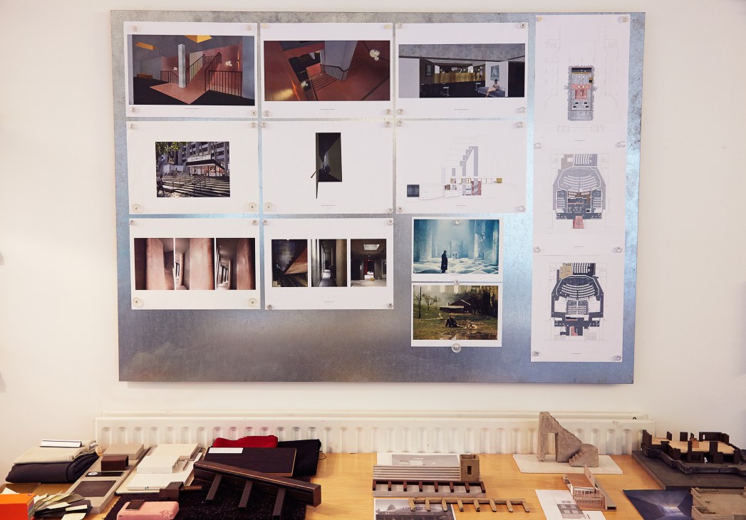 Architect's mood board displaying design inspiration including film stills, renderings, and architectural plans pinned to wall above desk.