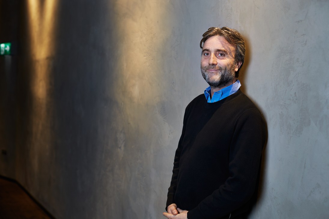Philip Knatchbull, boss of Curzon film group, stands against a concrete wall wearing a black sweater and blue shirt.