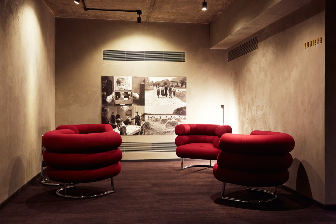Red Bibendum chairs in a concrete lounge with black-and-white film stills on the wall.
