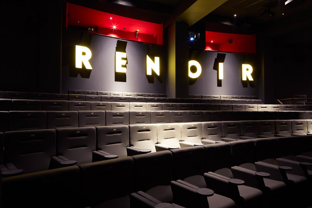Cinema auditorium with illuminated RENOIR sign above rows of dark seats and red lighting.