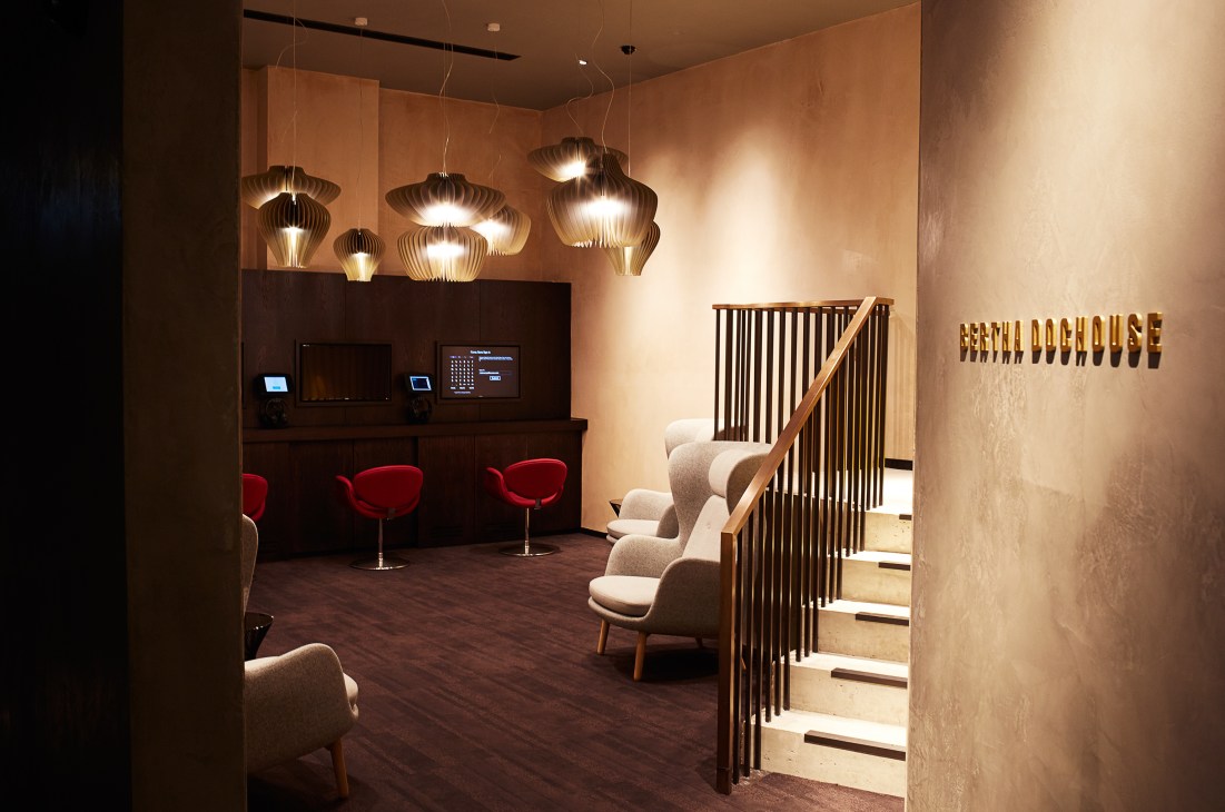 The Bertha DocHouse lounge features cream chairs, a bar with red stools, pendant lights, and brass signage.