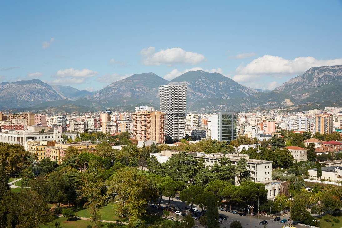 Downtown Tirana cityscape with mountains in background and modern white building in center.