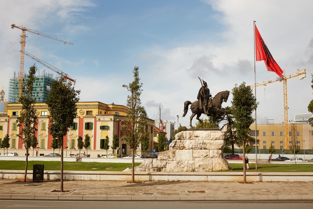Statue of Skanderbeg on horseback in Tirana's Skanderbeg Square with colorful buildings and Albanian flag