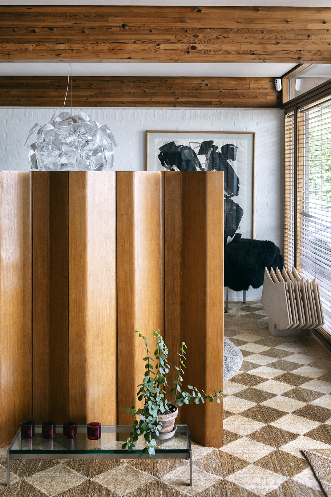 Untreated wooden interior wall panels with aged patina in a modernist home, featuring a small glass table and potted plant.