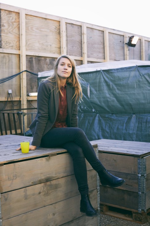 Sara Hjort Ditlevsen sits on a wooden platform on a film set, wearing dark clothing and a cardigan.