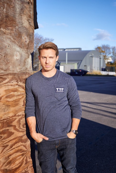 Actor Johannes Lassen stands against a wooden post at the Filmstationen lot, wearing a grey long-sleeved shirt.