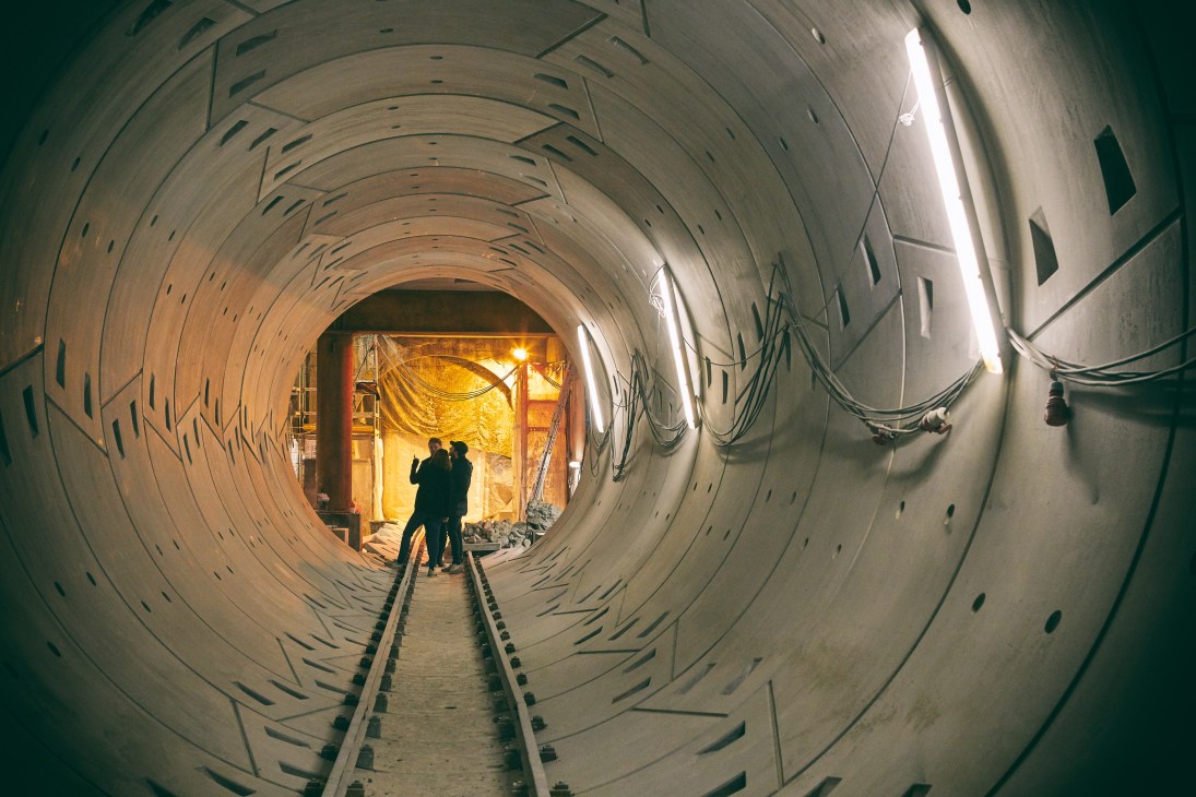 Crew members inspect a replica subway tunnel set with fluorescent lighting and railway tracks.