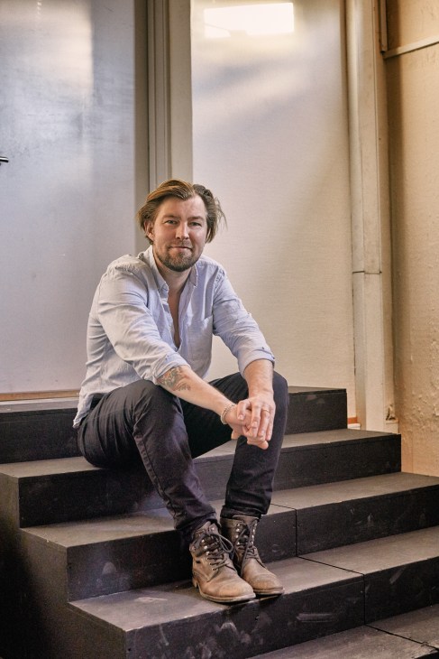 Producer Morten Kjems Juhl sitting on steps wearing a light blue shirt and dark jeans.