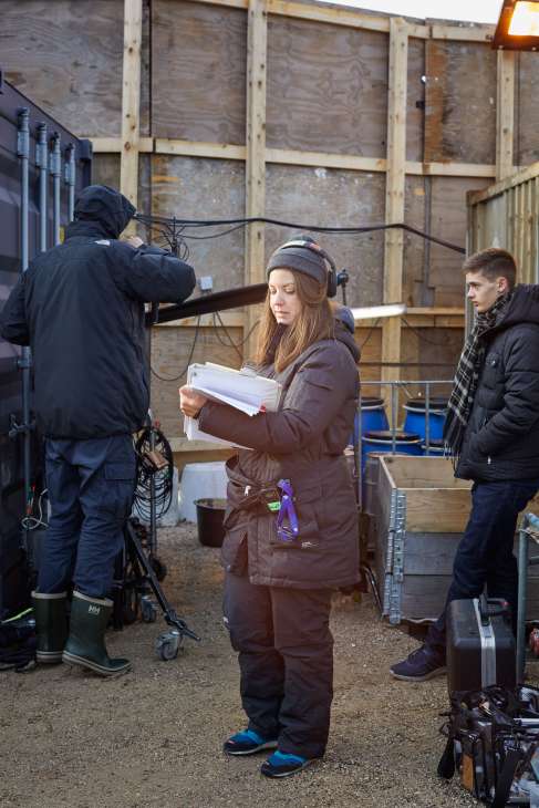 Crew member in brown jacket holding continuity notes on set of Below the Surface production.