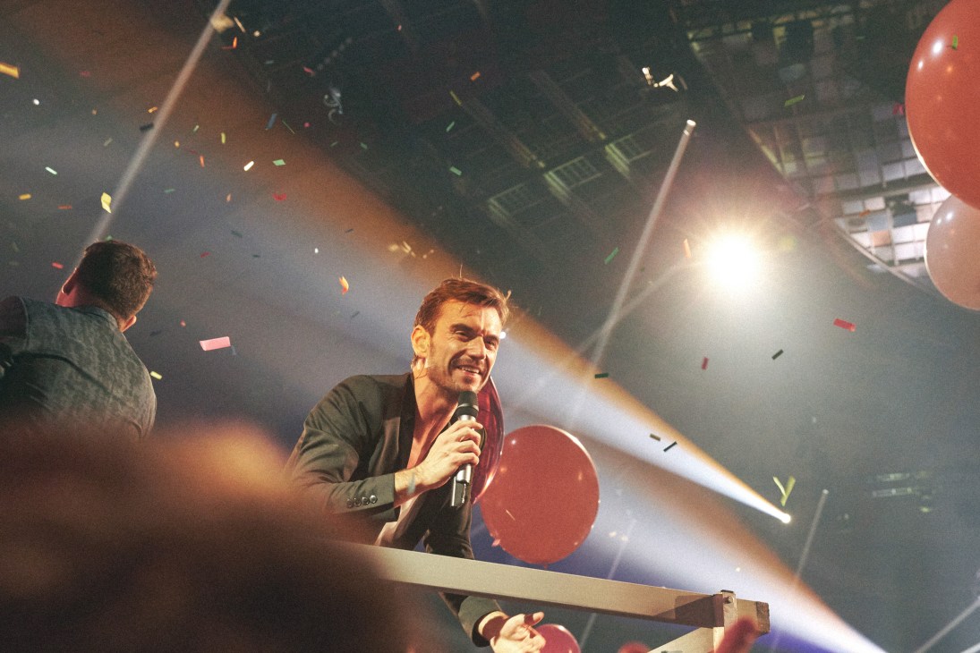 Florian Silbereisen on stage with microphone amid confetti and stage lighting at Schlagerbooom