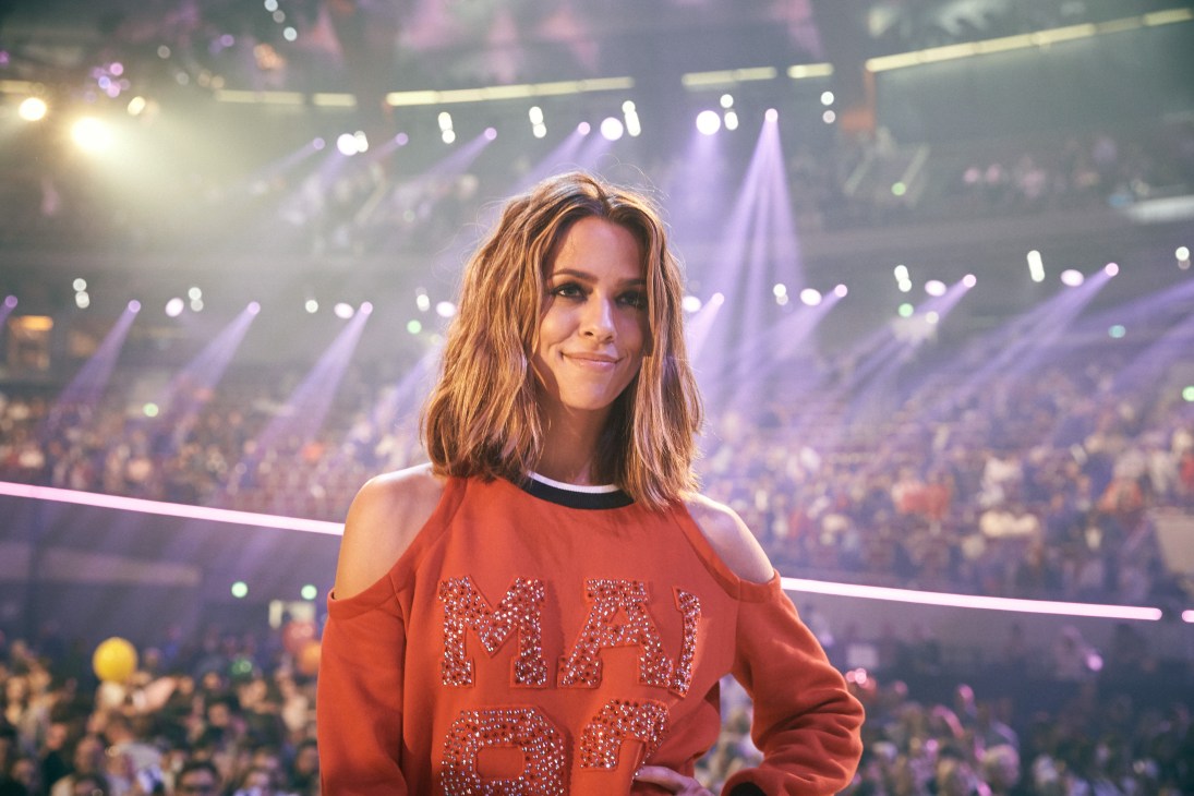Vanessa Mai performs on stage in an orange cold-shoulder top at Schlagerbooom concert.