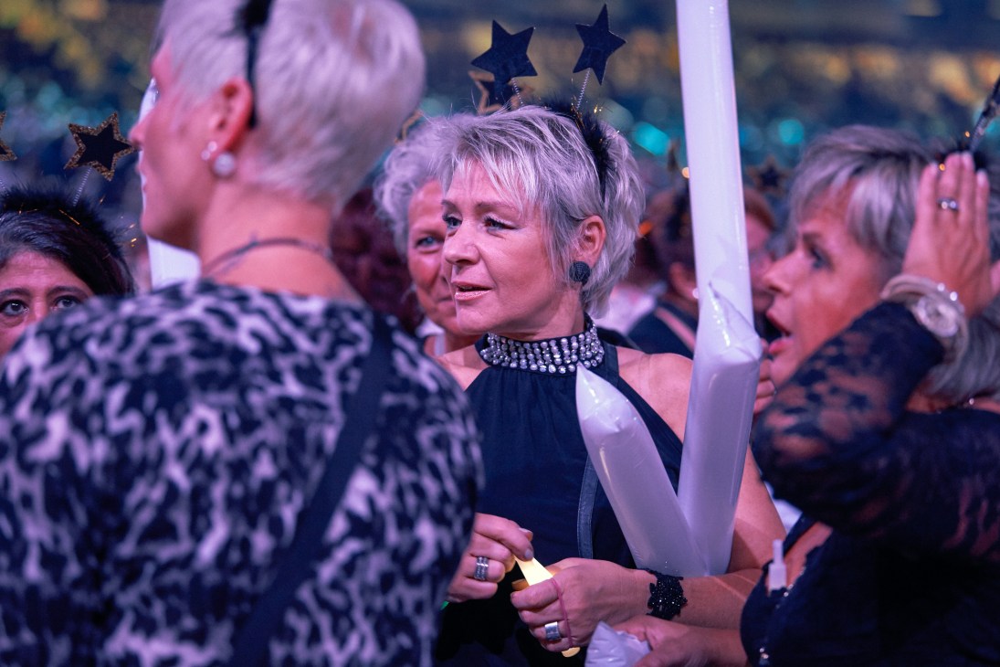 Woman with short grey hair and studded choker at Schlagerbooom event surrounded by crowd members wearing star accessories.
