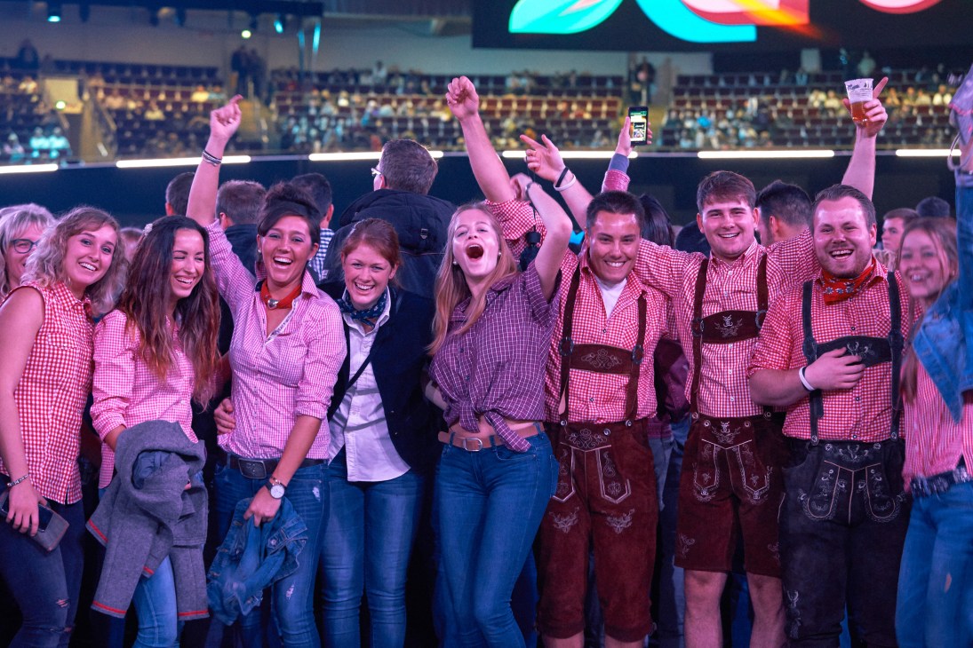 Enthusiastic schlager fans in traditional German attire celebrate at Schlagerbooom event, raising fists and smiling at concert venue.