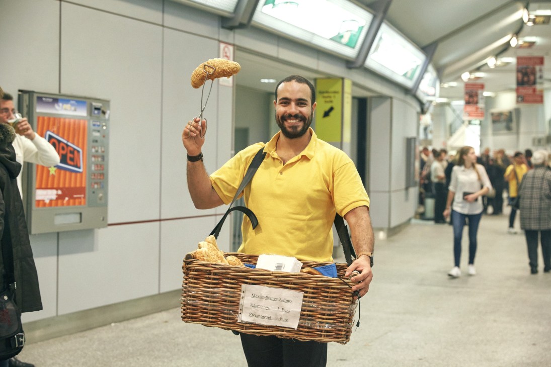 Man in yellow shirt holds wicker basket of bread in modern train station corridor.
