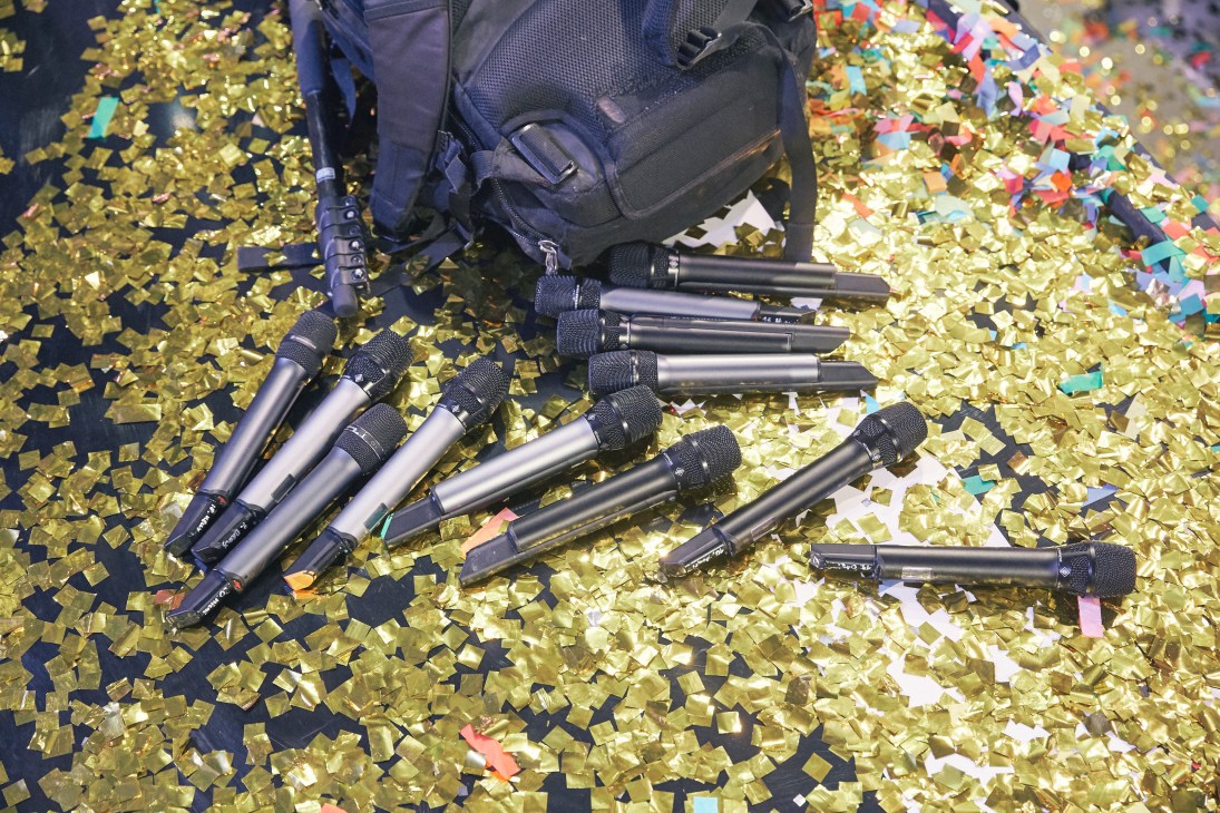 Wireless microphones and audio equipment scattered on confetti-covered stage floor.