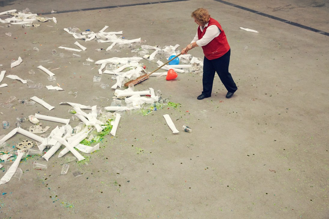 Woman in red vest sweeping debris and litter on an empty venue floor