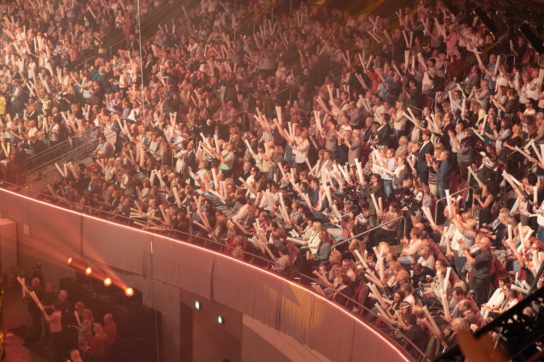 A packed concert hall with thousands of spectators with raised arms cheering at a Schlagerbooom event.