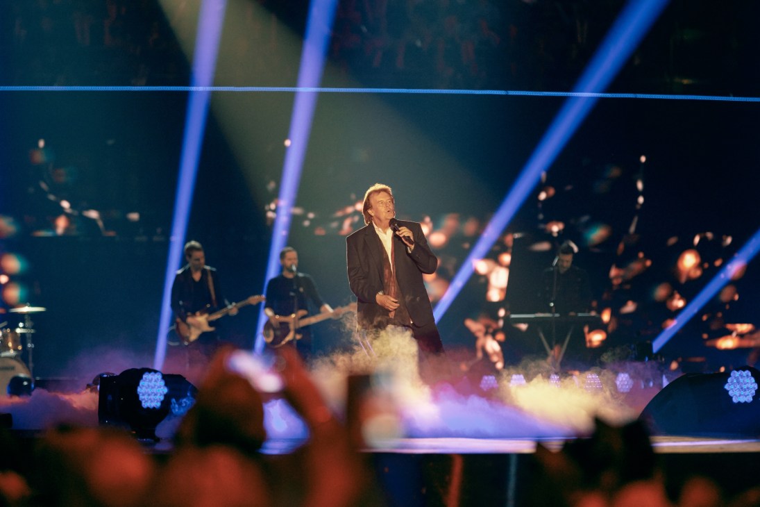 Howard Carpendale performing on stage at Schlagerbooom concert with blue stage lighting and dry ice effects.