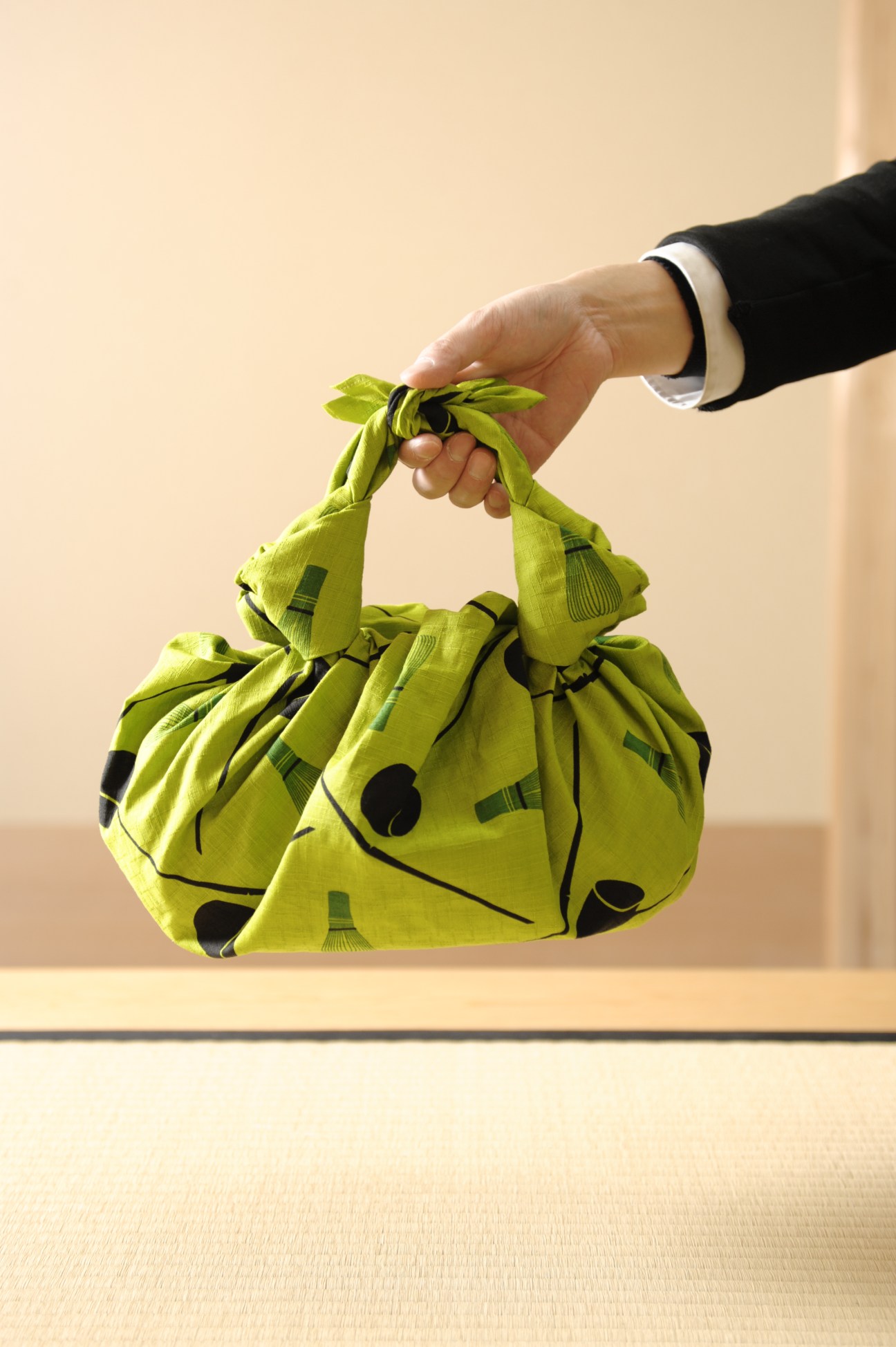 Hand holding a lime-green furoshiki cloth tied into a bag with geometric patterns in black.