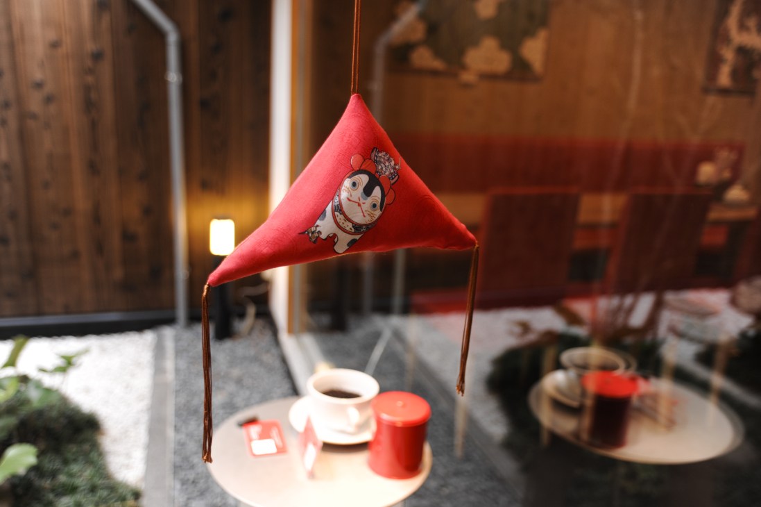 Red fabric pennant flag with illustrated cat motif hanging above a miniature table setting in Eirakuya tea shop.
