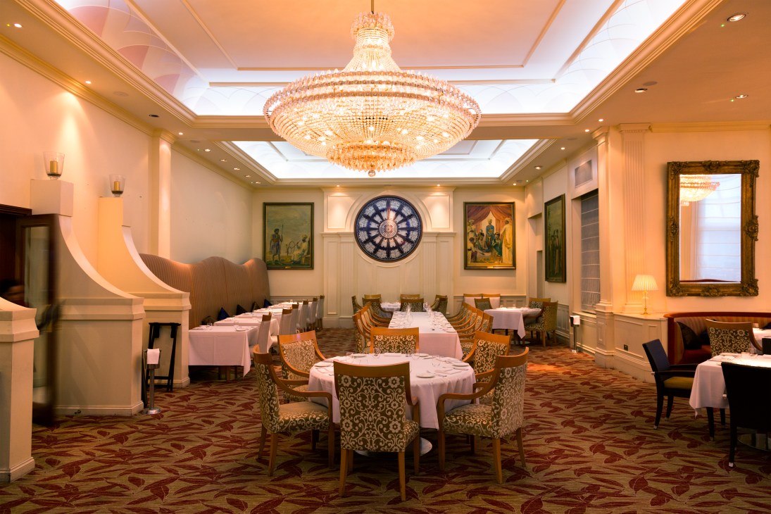 Ornate dining room with crystal chandelier, pink tablecloths, patterned chairs, and Indian artwork at Bombay Brasserie.