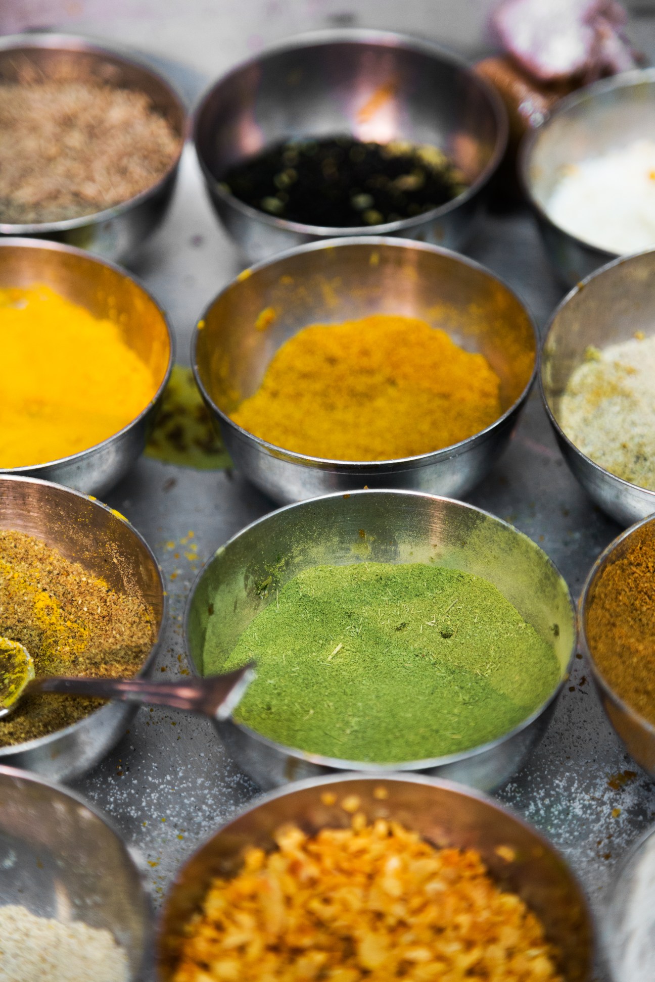 Metal bowls containing various colorful herbs and spices including turmeric, coriander and cumin.