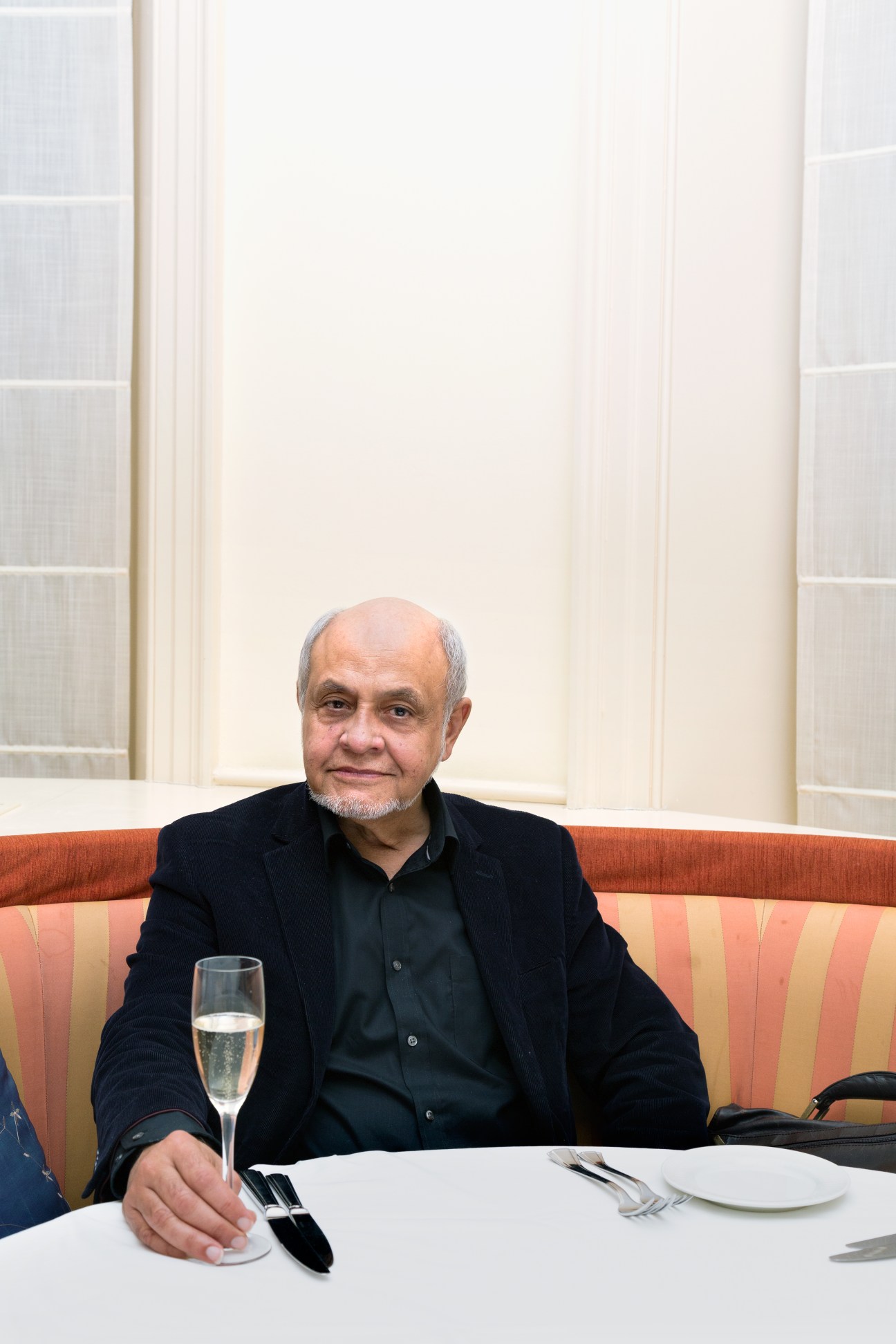 Cecil Balmond seated at a dining table with a glass of champagne in front of him.