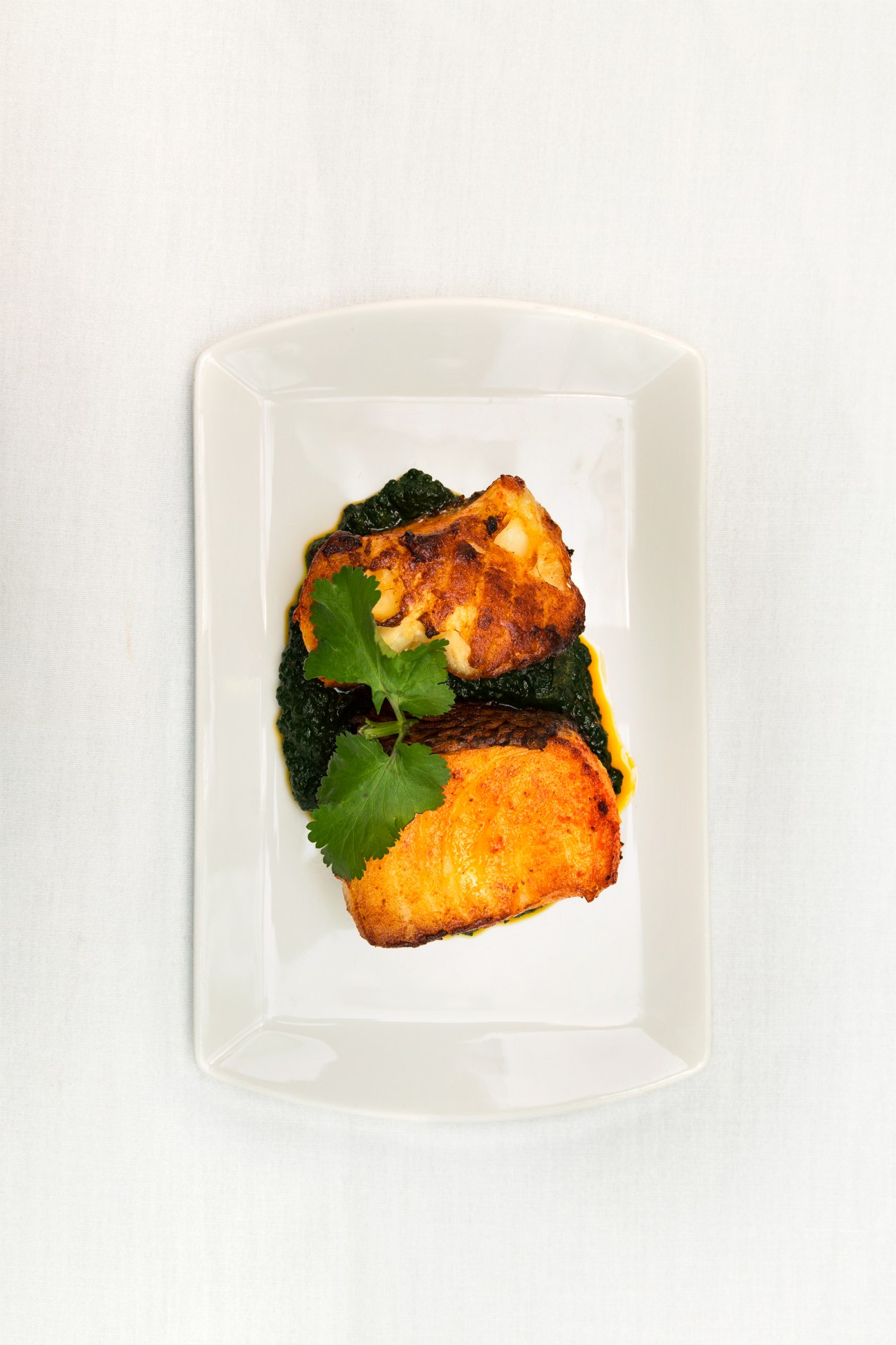 Masala sea bass topped with coriander and served on a spinach-and-mushroom base on a white plate.