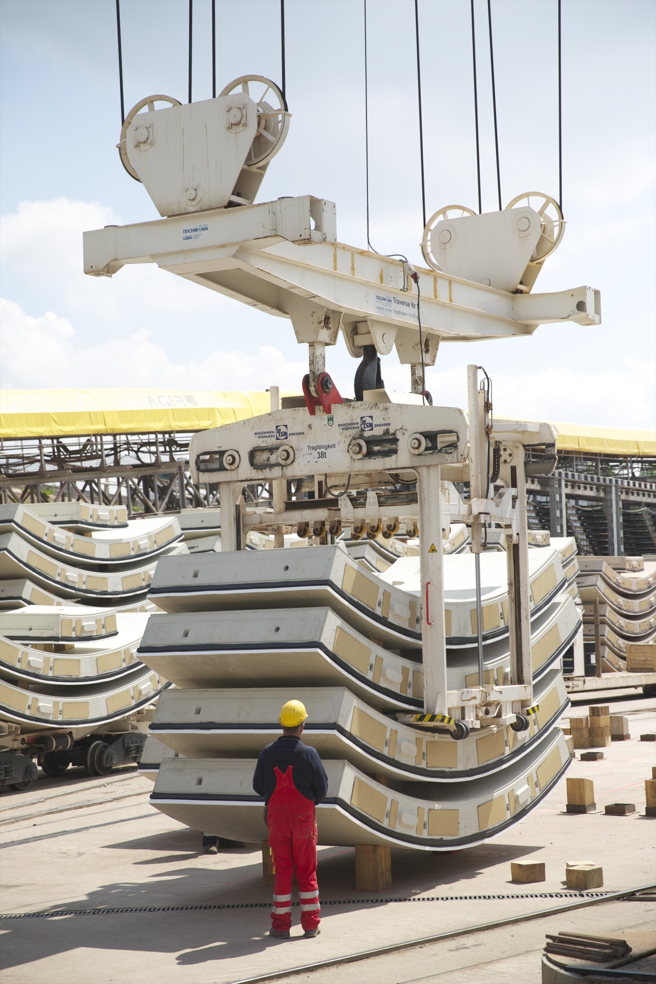 Worker in red safety gear observing large curved concrete tunnel shell segments being lifted by crane at industrial site.