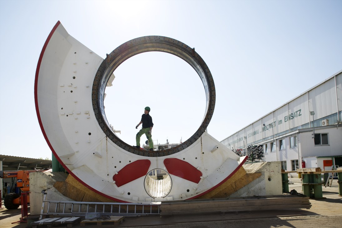 Worker standing inside large circular tunnel boring machine cutting head at Herrenknecht factory in Schwanau.