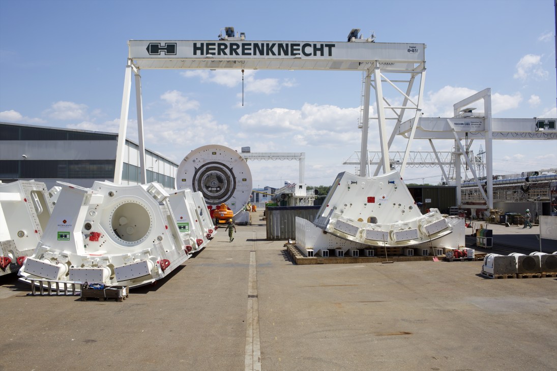 Large tunnel boring machine components displayed at Herrenknecht's Schwanau factory under a gantry crane.