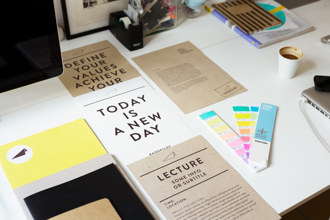KaosPilot's new visual identity materials including branded documents, color swatches, and design elements on a desk.