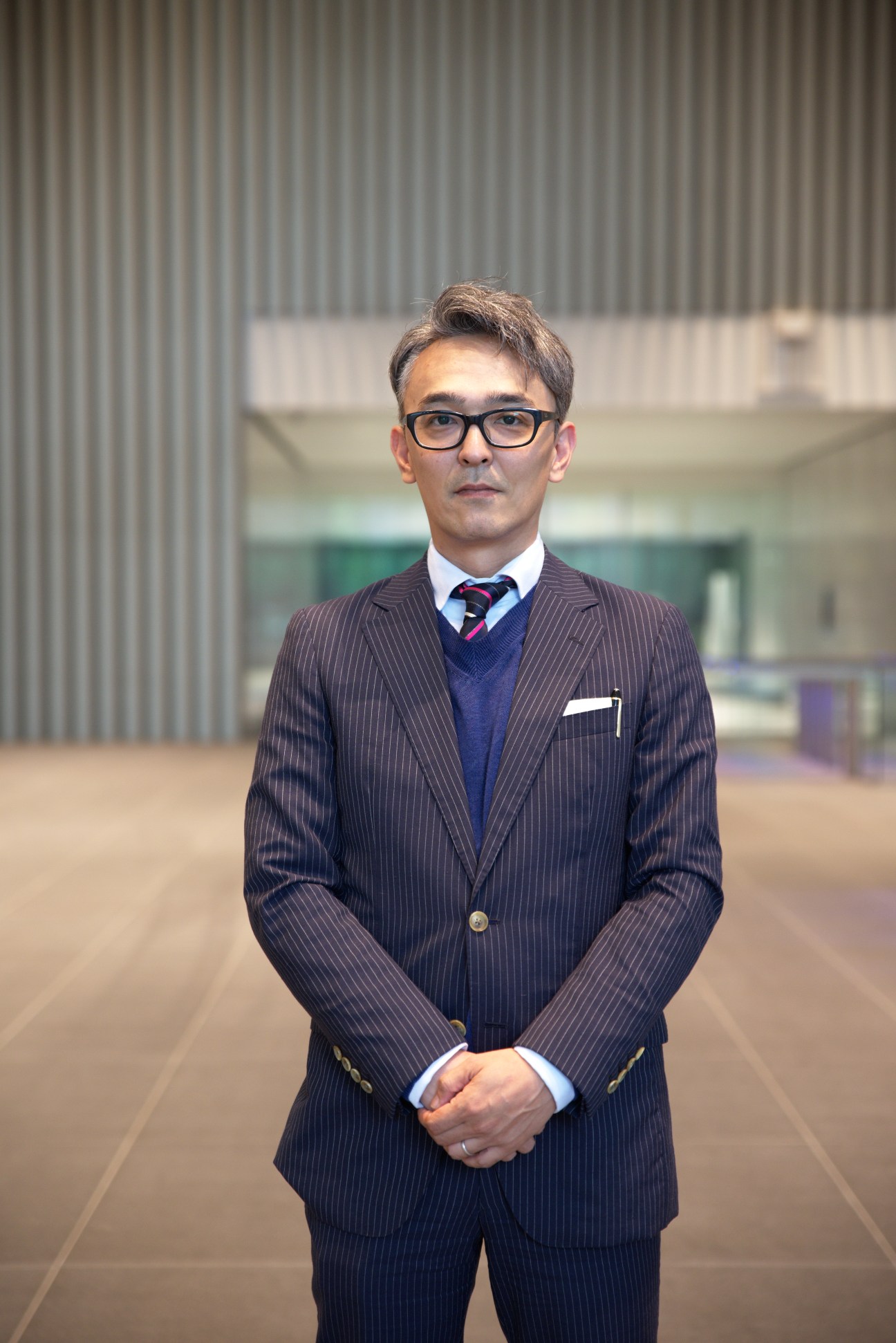Motohiro Nagashima of Seibu Properties stands in business attire in a modern corridor.