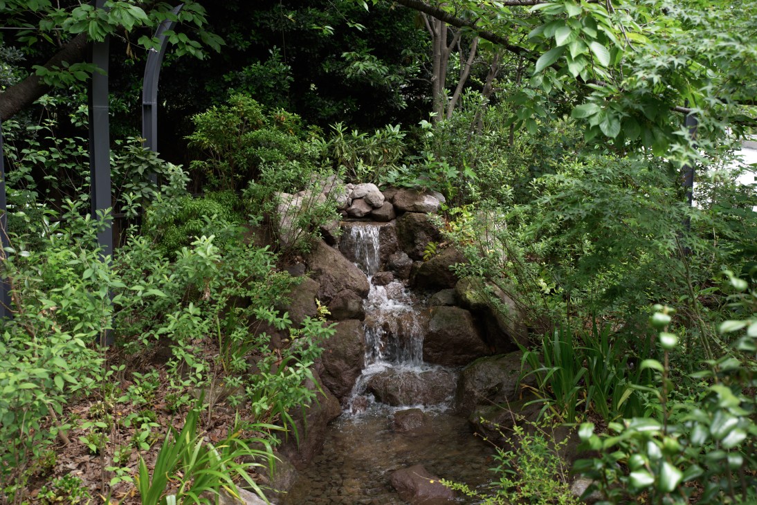 A tiered stone waterfall surrounded by lush green foliage in a garden setting.