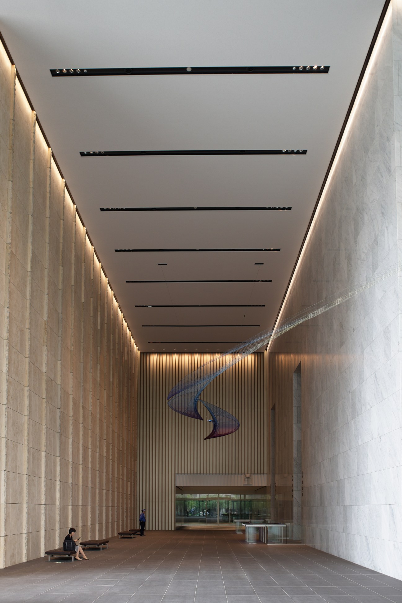 Minimalist hallway with linear ceiling lights and textured walls leading to a ground-floor entrance of Tokyo Garden Terrace Kioicho.