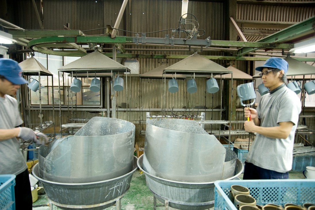 Workers inspect large steel pots during the first stage of enamelling at Noda Horo factory.