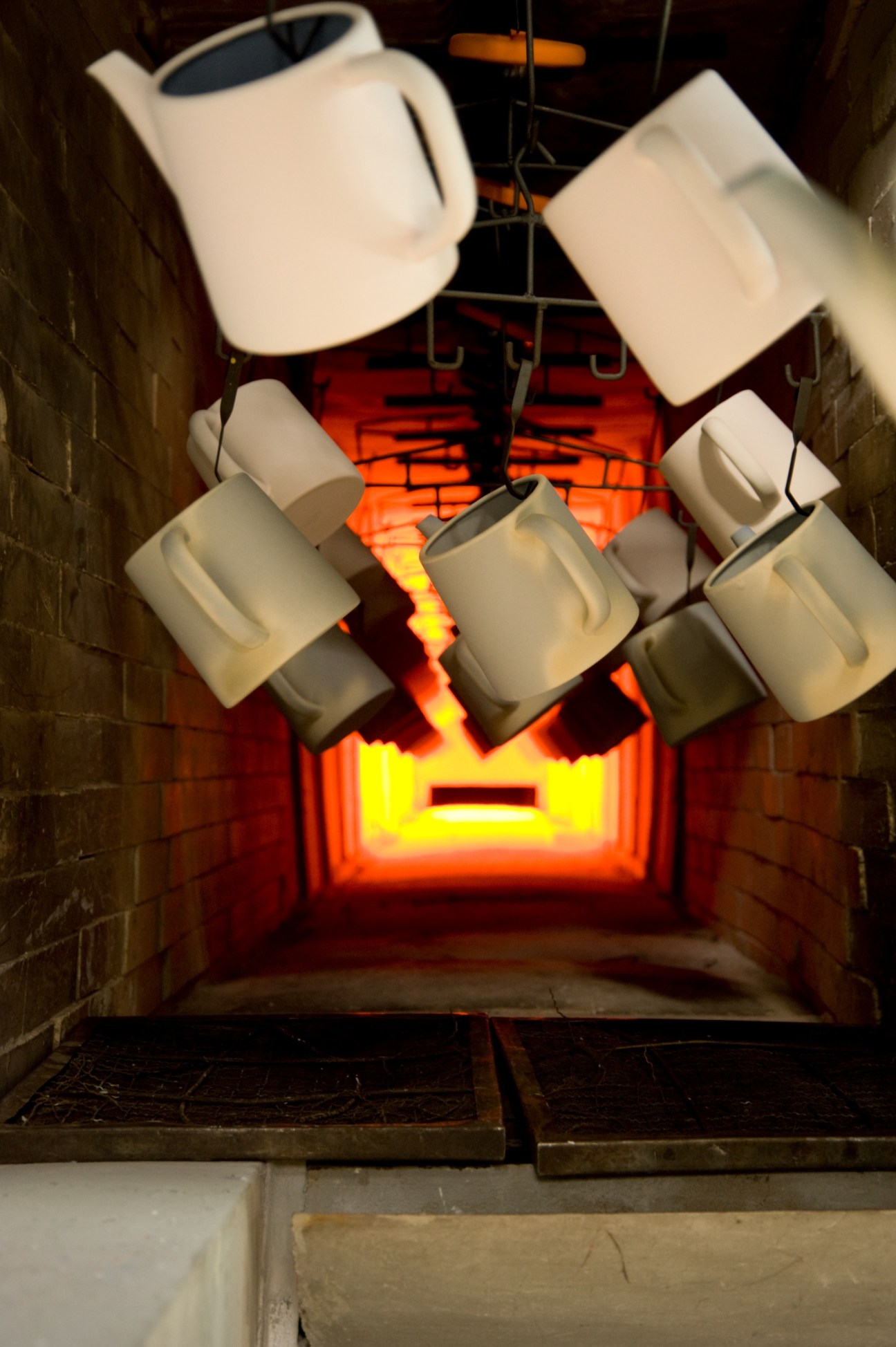 White enamel pots suspended in a kiln with glowing orange and yellow heat below.